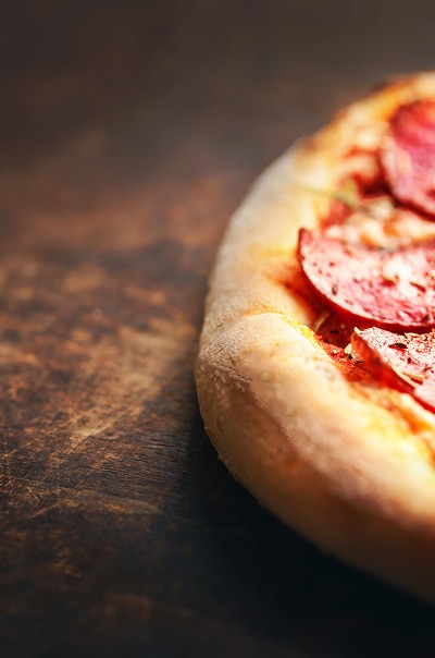 Pizza pepperoni croustillante sur bois rustique Gros plan d'une pizza pepperoni chaude, mettant en évidence sa croute épaisse et dorée. Elle repose sur une surface en bois sombre et rustique.