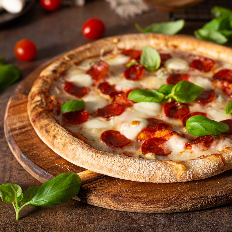 Pizza Pepperoni Classique : Recette avec Mozzarella et Basilic Délicieuse pizza artisanale avec croûte gonflée, garnie de pepperoni piquant, mozzarella fondante et feuilles de basilic frais.